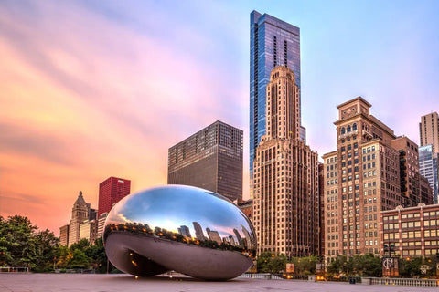 Cloud Gate (The Bean) sculpture reflecting city buildings under a colorful sunset sky in downtown Chicago, with tall skyscrapers and historic architecture in the background.