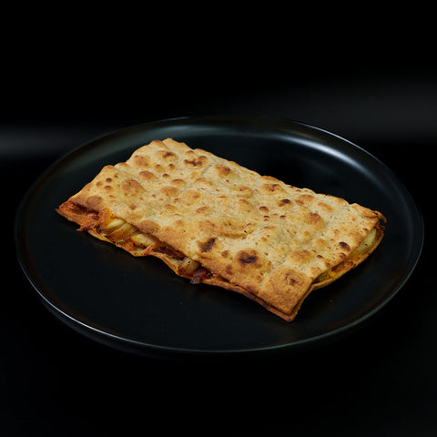 The Strongsville Chicken Ranch Fold is a rectangular toasted flatbread sandwich with a golden-brown crust and visible fillings, offering a high-protein meal. It’s served on a black plate against a black background.