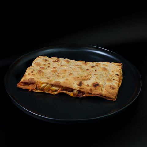 The Strongsville Chicken Ranch Fold is a rectangular flatbread sandwich with a golden, slightly crispy top, filled with cheese, vegetables, and HALAL turkey bacon, served on a plain black plate against a dark background.