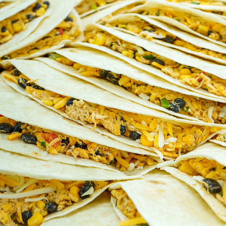 A close-up view of several soft tortillas filled with shredded chicken, black beans, corn, cheese, and diced vegetables, arranged in rows and ready for baking or serving.