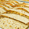 Rows of folded flatbread quesadillas filled with melted cheese and vegetables, stacked closely together on a tray.
