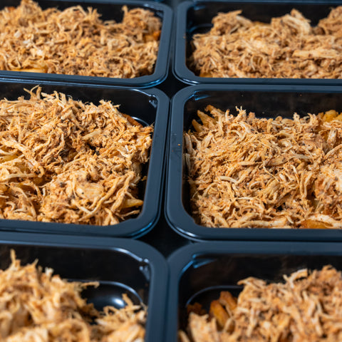 Close-up of several black meal prep containers filled with shredded cooked chicken, arranged in a grid pattern.