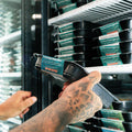 A person with a tattooed hand selects a packaged meal labeled Crying Tiger Steak Bowl from a refrigerator shelf stocked with similar meals.