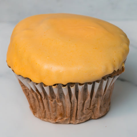 The Buffin Muffin - Buffalicious Baddie, a blueberry lemon cheesecake muffin with smooth yellow cheese, sits in a paper liner on a white surface—a tasty, high-protein snack perfect for the gym.