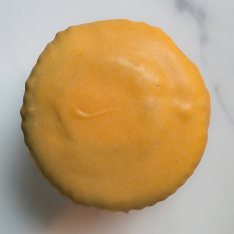A round muffin birds eye view with a smooth, icing-coated surface, viewed from above on a light marble background.
