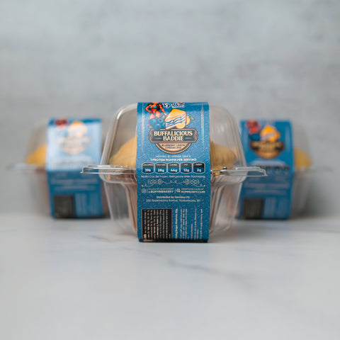Three clear plastic containers of Buffalicious Baddie savory hot pockets are arranged on a light surface, with one container in focus and two blurred in the background, all with blue packaging labels.