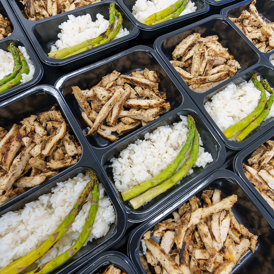 Meal prep containers filled with grilled chicken strips, white rice, and asparagus spears, neatly arranged in rows.