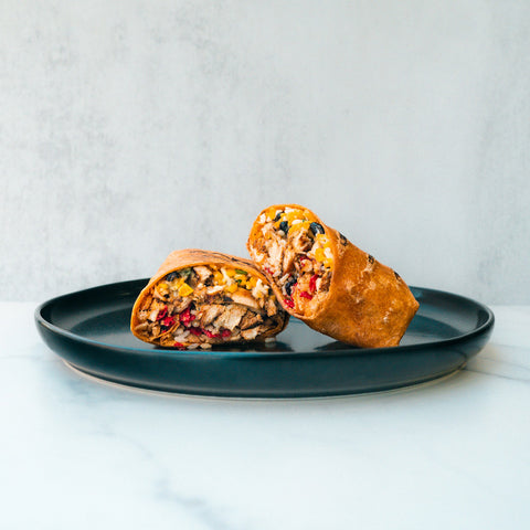 The Hey Arnold Burrito, packed with high-protein chicken, beans, corn, and red peppers, is sliced in half to reveal its hearty filling on a dark plate—making it an ideal post-workout meal.