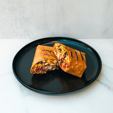 The Hey Arnold Burrito, packed with chicken, corn, black beans, and veggies, is sliced in half and served on a black plate—an ideal high-protein meal for post-workout satisfaction.