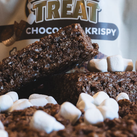 Close-up of a Chocolate Buff Krispy Treat with mini marshmallows scattered around, and a partially visible package labeled Chocolate Buff Krispy Treat in the background—a delicious guilt-free snack.
