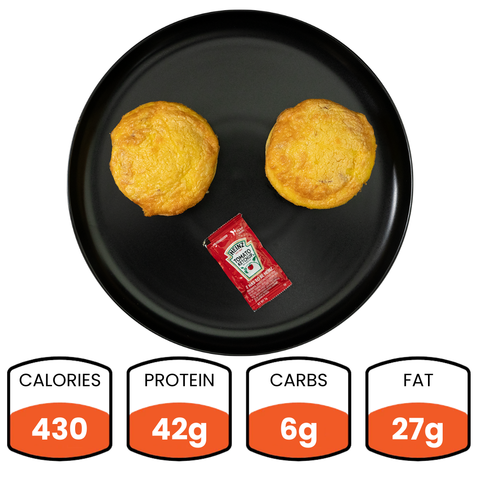Two Bacon Cheddar Egg Muffins with a ketchup packet are served on a black plate—ideal for healthy breakfast meal prep. Nutrition: 430 calories, 42g protein, 6g carbs, and 27g fat.