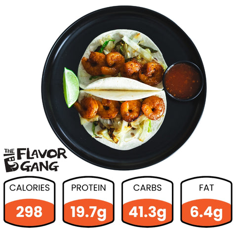 A plate with two shrimp tacos, garnished with lime and served with a side of Flavor Gang Bahaha Sauce, with nutritional information displayed.