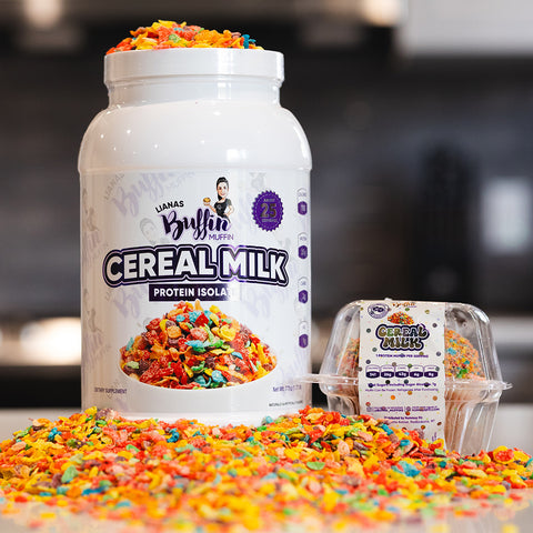 A large white container labeled Lianas Buffin Muffin - Protein Isolate sits beside a smaller cup, both surrounded by colorful, crunchy cereal pieces, showcasing its dessert-inspired flavors on a kitchen counter.