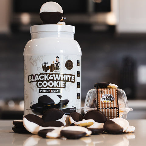 A container of Lianas Buffin Muffin - Protein Isolate, inspired by black and white cookies, sits on a kitchen counter surrounded by cookies and a small clear package with more cookies nearby.
