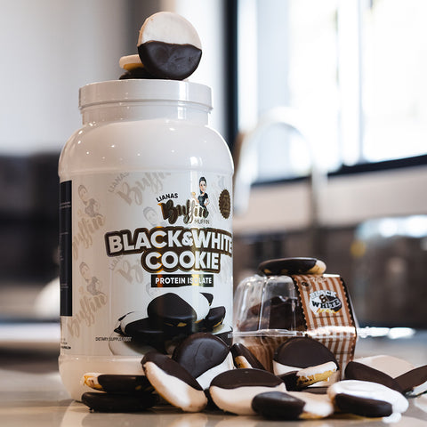 A large container labeled Lianas Buffin Muffin - Protein Isolate is surrounded by muffins, emphasizing its bakery-inspired flavor, with a small muffin pack and a kitchen sink blurred in the background.