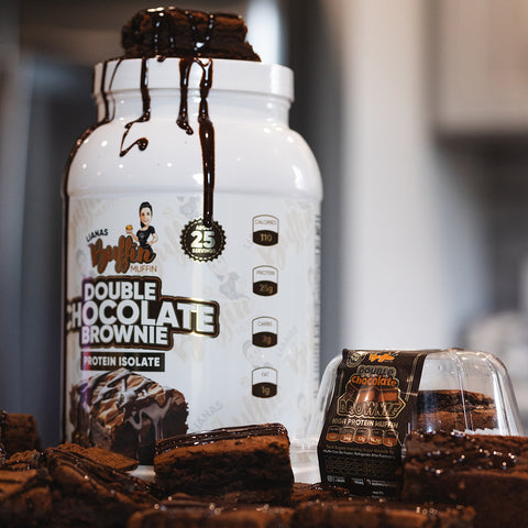 A large white container of Lianas Buffin Muffin - Protein Isolate (Subscription), dessert-inspired with a chocolate drizzle, is surrounded by brownies. A packaged brownie in the foreground highlights this decadent protein snack.