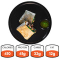 A black plate holds a halved Grilled Chicken Pesto Wrap packed with veggies and protein, plus a green dipping sauce. Nutrition: 410 calories, 41g protein, 32g carbs, and 12g fat—making it a healthy meal prep choice.