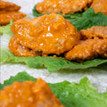 Close-up of saucy buffalo chicken wings placed on fresh green lettuce leaves, with more wings visible in the background.