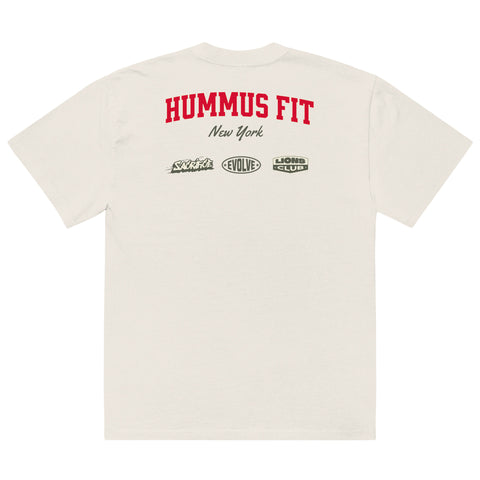 Back view of an off-white t-shirt with HUMMUS FIT in large red letters, New York below in black script, and three sponsor logos—Slickfade, EVOLVE, and LIONS CLUB—printed underneath.