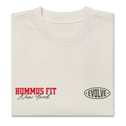 A folded off-white t-shirt with HUMMUS FIT New York in red and black text on the left chest and EVOLVE in an oval logo on the right chest.