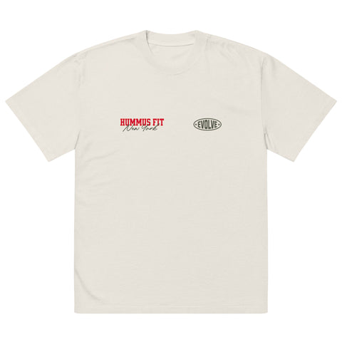 A plain off-white T-shirt featuring “HUMMUS FIT New York” in red and black text on the left chest, and an oval-shaped “EVOLVE” logo in black on the right chest.