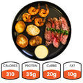 A plate with surf and turf meal consisting of grass-fed Angus flank steak, juicy shrimp, seasoned Idaho potatoes, and a creamy Dijon mustard sauce, with labels indicating calorie count, protein, carbs, and fat content.