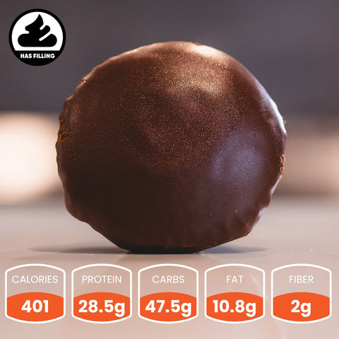 A Buffin Muffin Twin Roll, a round, chocolate-covered snack with filling inside, rests on a smooth surface. Nutrition: 401 calories, 28.5g protein, 47.5g carbs, 10.8g fat, and 2g fiber.