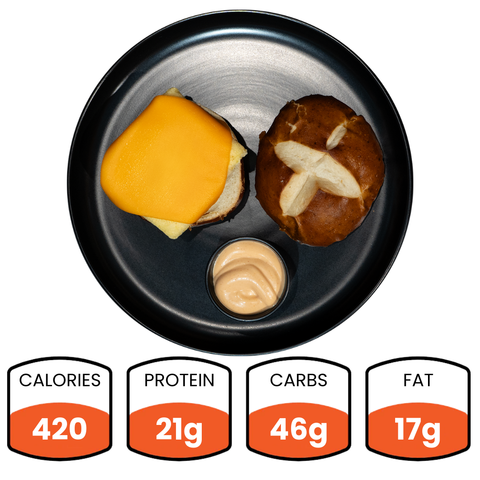 A black plate holds the Vegan Breakfast Sandwich with a pretzel bun, cheeseburger patty, and a cup of sauce. This high-protein breakfast packs 21g protein, 46g carbs, and 17g fat in just 420 calories. Nutritional info below.