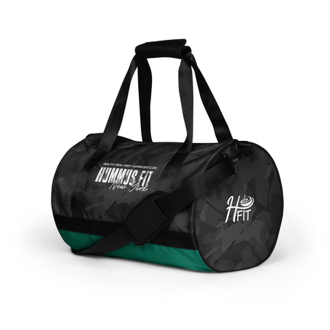 The Hummus Fit Cylinder Black Camo Gym Bag features water-resistant black and dark green camo, black straps and shoulder pad, plus HUMMUS FIT New York and H FIT logos in white on the side and end panels.