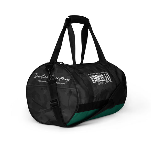 The Hummus Fit Cylinder Black Camo Gym Bag features an all-over dark camo print, black handles, a green stripe at the base, and white HUMANS ARE New York and Search for Everything text on the side.