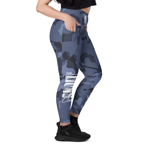 A woman in profile wears Blue Camo Leggings With Pockets, a black crop top, and black sneakers. Her left hand is in her pocket, and only the lower half of her face is visible.