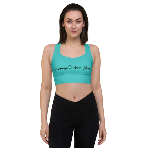 A woman with shoulder-length dark hair models the Hummus New York Sports Bra in turquoise and black leggings, standing facing forward against a plain white background with her arms at her sides.