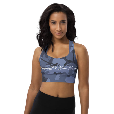A woman with medium-length dark hair wears the Blue Camo Sports Bra and black leggings, standing against a plain white background and looking at the camera.