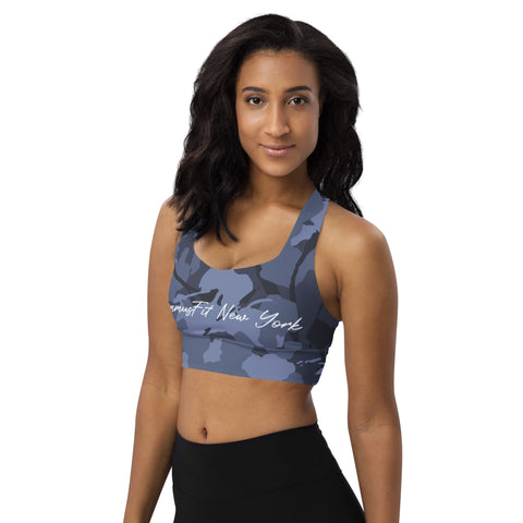 A woman with long dark hair, wearing the Blue Camo Sports Bra and black leggings, stands against a plain white background, looking confidently at the camera.