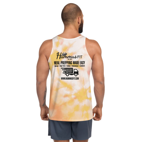 A man with a buzz cut, wearing a relaxed fit Pink & Gold Tank Top featuring Hummus Fit and a meal prep service ad on the back, pairs it with shorts and stands against a plain white background.