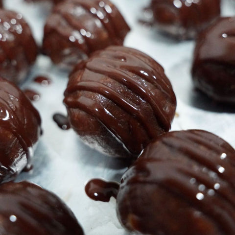 Close-up of 3 Banana Chocolate Protein Poppers (Subscription) drizzled with glossy chocolate sauce on a white surface—ideal for healthy snacking.