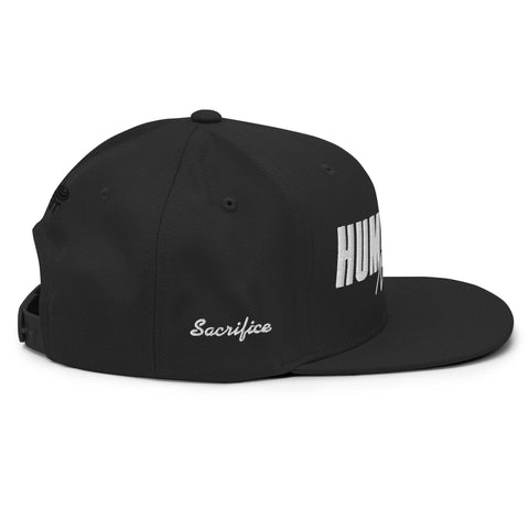 The Black Snapback Hat features bold white HUM lettering on the front and Sacrifice in white cursive on the side. Its adjustable snapback gives a classic fit and comfortable style for anyone.