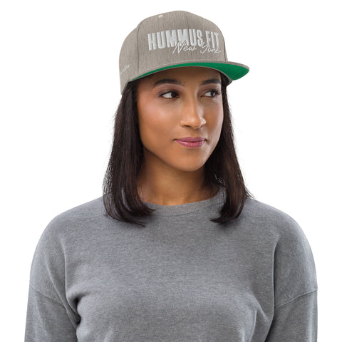A woman in a gray Heather Snapback Hat with adjustable snap closure and a gray sweater looks to the side against a plain white background.