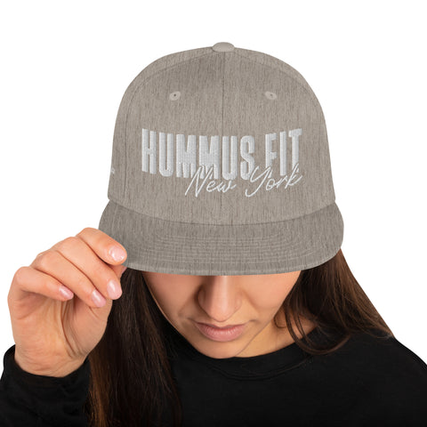 A person wears a Heather Snapback Hat with a flat brim, tilting it to partly cover their face. The classic fit cap sits over long brown hair, combining style and comfort.