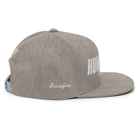 The Heather Snapback Hat is a gray, classic fit cap with Sacrifice embroidered in white on the side, featuring a flat brim and an adjustable light gray snap closure for a comfortable, custom fit.