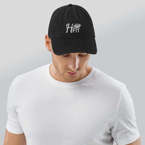 A man wearing a plain white t-shirt and the H-Fit Black Denim Hat, featuring an embroidered swirl logo and adjustable strap, looks down against a neutral gray background.