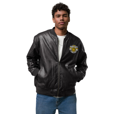 A young man stands hands-in-pockets against a white background, wearing the Lions Club Leather Bomber Jacket—a black PU jacket with a yellow and white embroidered chest patch—paired with a white t-shirt and blue jeans.