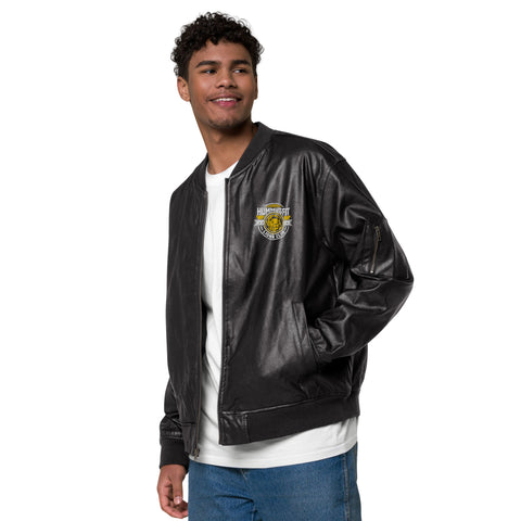 A young man with curly hair wears the Lions Club Leather Bomber Jacket, featuring a small embroidered patch on the left chest, over a white T-shirt and blue jeans. He is smiling and looking to his left.