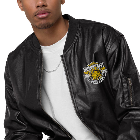 Someone wears the Lions Club Leather Bomber Jacket, featuring the Hummusfit Lions Club logo on the chest, styled over a white t-shirt and a thin chain necklace. Only the lower half of their face is visible.