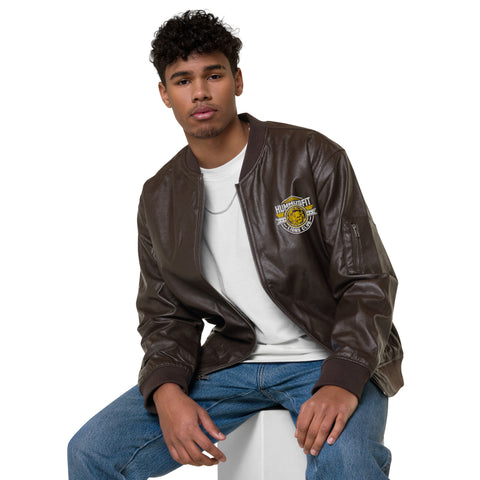 A young man with short curly hair wears the Lions Club Leather Bomber Jacket over a white t-shirt and blue jeans. Seated against a plain white background, he looks at the camera with a neutral expression.