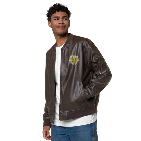 A young man with curly hair wears the Lion’s Club Leather Bomber Jacket—a brown PU leather piece with a small chest patch—over a white T-shirt and blue jeans. He smiles and looks to the side against a white background.