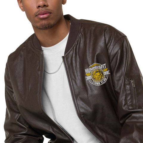 A person wears the Lions Club Leather Bomber Jacket with a Hummusfit Lions Club patch, layered over a white shirt and silver chain necklace; the photo shows them from shoulders to mid-chest.