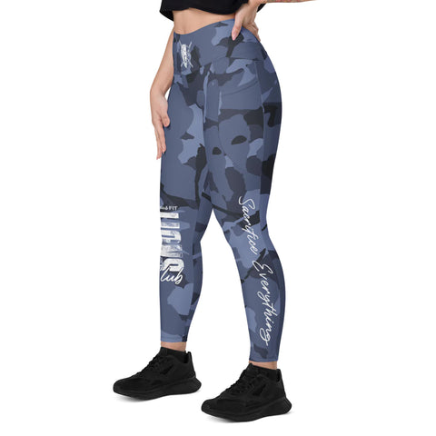 A woman stands in a side pose with one hand on her hip, wearing Blue Camo Leggings With Pockets, a black crop top, and black sneakers against a plain white background.