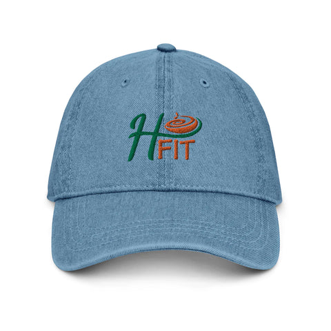The H-Fit Blue Denim Hat is made from 100% cotton in light blue, with H FIT embroidered in green and orange plus a swirl design above. It features a curved brim, visible stitching, and an adjustable strap for comfort and style.