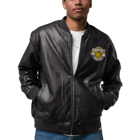 A person wearing a Lions Club Leather Bomber Jacket in black PU leather with hands in pockets, featuring a Lions Club patch on the left chest, over a white shirt and blue jeans, standing against a white background.